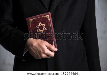 cropped view of young jewish man holding tanakh  Royalty-Free Stock Photo #1599944641