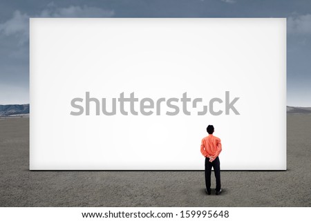 Asian businessman looking at empty billboard under cloudy sky