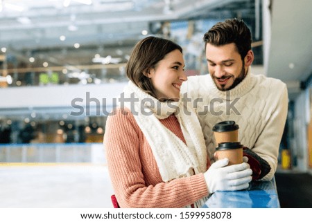 smiling couple holding coffee to go on skating rink