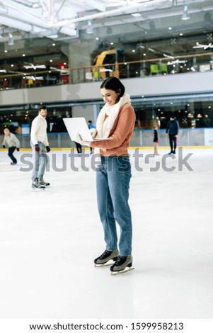 beautiful girl using laptop on skating rink with people