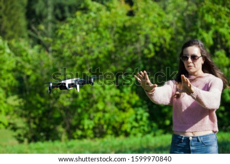 Walk with a drone. A young woman in black glasses launches a low flying drone. Reaches out to a low flying drone, catches. Blurred background. Front view.