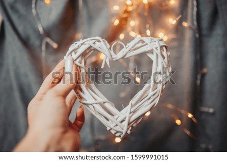 Saint Valentine's day card. Woman holds big white wooden heart with bright bokeh. Wicker heart with garland lights.
