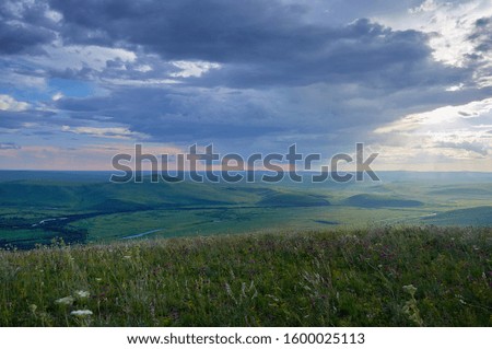 Far green hills and flowering steppe under the sunset sky during the rain.