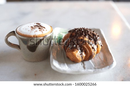 Hot coffee with milk foam in a cup And croissants or bake bread With chocolate in a white tile dish White granite table top