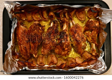 A dish with roasted turkey wings on foil with baked apples for the whole frame.