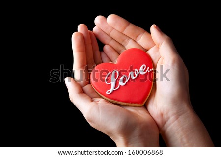 Red cookie heart with love word holding by woman isolated on black background for Valentines Day
