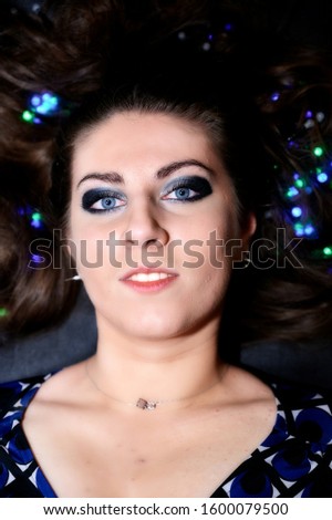 Large art portrait of a pretty brunette woman with excellent make-up with artificial multi-colored light in her hair.
