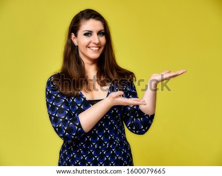Portrait of a pretty brunette woman with a beautiful hairstyle and with excellent makeup in a dark blue blouse on a yellow background. It stands showing hands with a smile in front of the camera.