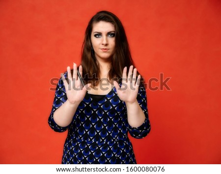 Portrait of a pretty brunette woman with a beautiful hairstyle and with excellent makeup in a dark blue blouse on a red background. He stands with a smile and shows his hands with emotions.