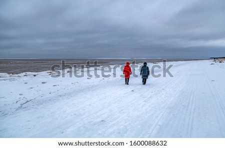 Two people walk along the snowy coast of the sea, enjoying the winter landscape and the frosty air.