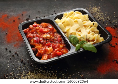 Dietetic catering, Chicken in Italian sauce with tagliatelle.
Ready dish in a black container. Composed take-out meal, diet catering. The container on a dark background. Royalty-Free Stock Photo #1600092364