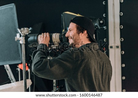 Side view of smiling handsome cameraman working in photo studio