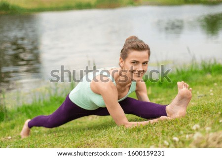 A young sports girl practices yoga on a green lawn by the river, assans posture. Unity with nature