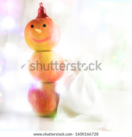 Concept of Sustainable, Zero waste, Vegan Christmas. Creative snowman from apples holding bag full of presents for Christmas on festive lights background.