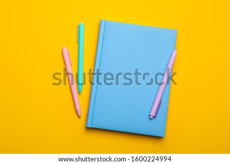 Light blue notebook and pens on yellow background, flat lay