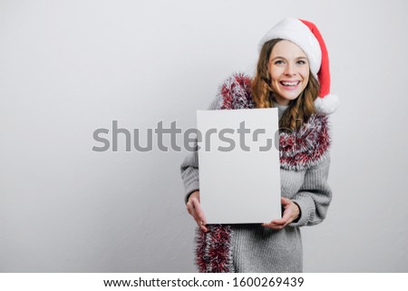 Happy girl in Santa hat with blank empty canvas board. Mockup poster for Christmas message. Copy space.
