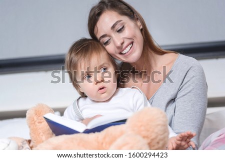 Young beautiful mother reads to baby the book before going to sleep in bed. Closeup picture, mother and son closeness concept
