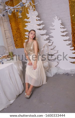 girl in a shiny evening dress. The girl is dreaming. Christmas Eve. Cozy holiday at the fur-tree with lights and gold decor. girl in a shiny dress on a background of Christmas background in the studio