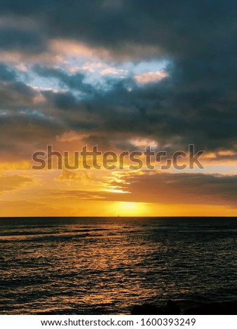 Beautiful sunset off the coast of Poipu on the island of Kauai in Hawaii, with the silhouette of a sailboat in the distance.
