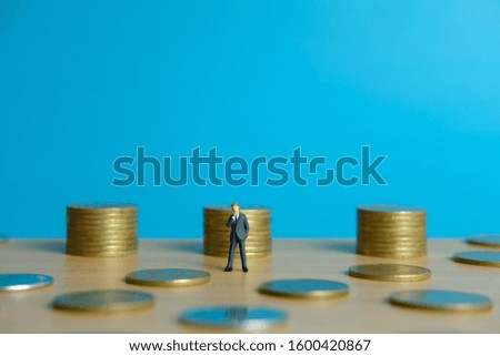 Miniature business concept - a businessman standing in front of stack of coin