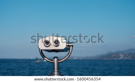 Public stationary binocular on sea shore, Coin operated metal binocular viewer on blurred background sea