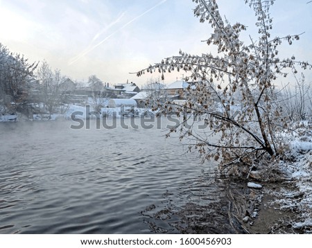 trees covered with frost near the unfrozen river in winter