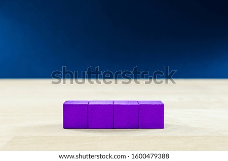 4 purple wooden blocks placed in a row on a solid oak table, with copy space, over blue background.