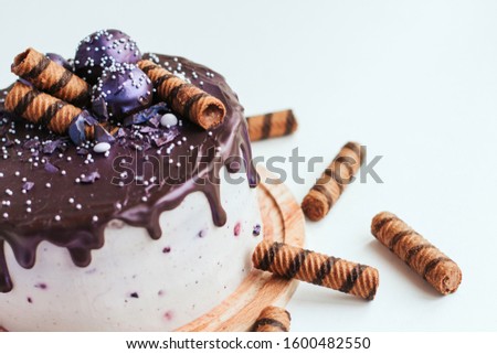 Purple glitter blueberry cake with chocolate glaze on a white background copy space. Homemade chocolate cake with blueberries and striped wafer rolls.