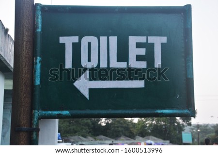 Sign of  toilet written in white color on a tin plate with green color background fixed on a thick iron pipe