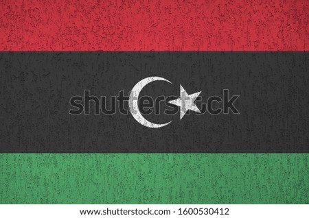 Libya flag depicted in bright paint colors on old relief plastering wall. Textured banner on rough background