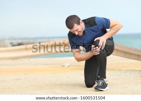 Painful runner complaining suffering knee ache after sport on the beach Royalty-Free Stock Photo #1600531504