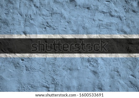 Botswana flag depicted in bright paint colors on old relief plastering wall. Textured banner on rough background