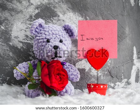 Bright plush toy, blooming red rose, white plaid and a note with a handwritten inscription. Studio photo. Close-up, indoors