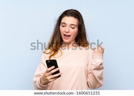 Young brunette girl over isolated blue background using mobile phone