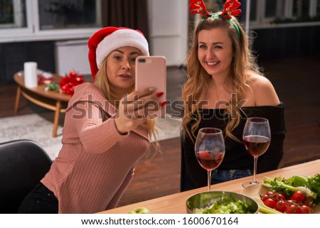 Young women celebrating New Year taking pictures of themselves while sitting in kitchen.