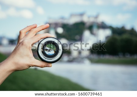 Hand holding camera lens with old city of Salzburg in it, close up