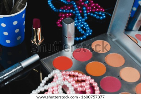 Creative concept beauty fashion photo of cosmetic product make up brushes kit with lipstick eye shadow and colored pearl beads on black background.