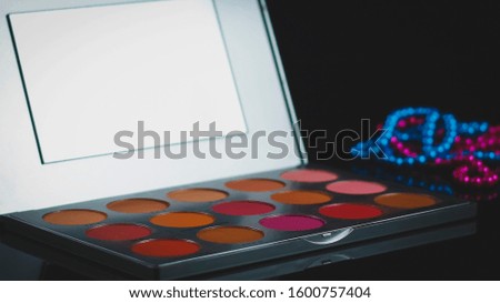 Creative concept beauty fashion photo of cosmetic product make up brushes kit with lipstick eye shadow and colored pearl beads on black background.