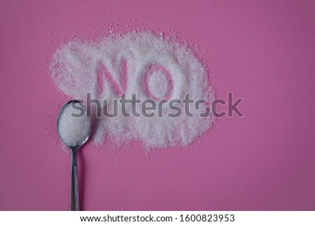 Word NO hand written on a heap of white sugar with full teaspoon of sugar on a pink background top view. Stop diabetes and excessive sugar intake concept. Healthcare, unhealthy diet concept. Royalty-Free Stock Photo #1600823953