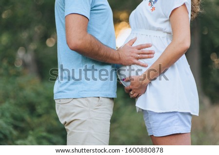 Pregnancy. Close-up of a man and a pregnant girl in a white dress holding hands on a big belly. Waiting for a miracle, baby. 9 months. Photography, concept, family.