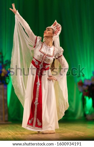 Young woman ballerina in a white suit with a crown on her head performs with a performance on stage in a theater