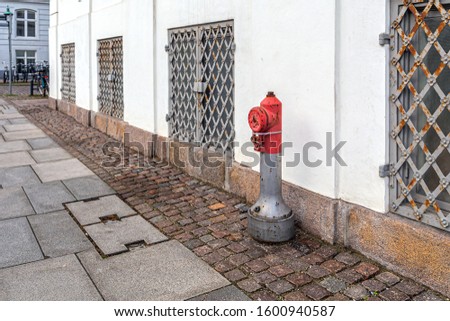 Fire hydrant on the pavement, near the wall of the house with barred Windows
