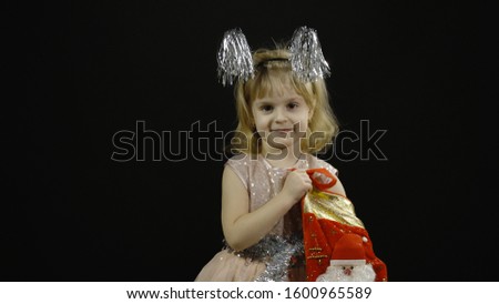 Happy beautiful little baby girl in glossy dress. Christmas concept. Looking for presents in christmas sock. Positive, pretty, four years old child make faces, dance and smile. Black background