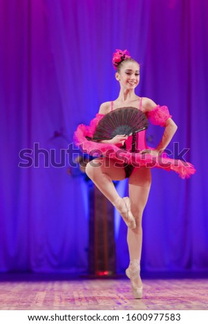 Young girl ballerina in a pink tutu performs with a performance on stage in a theater