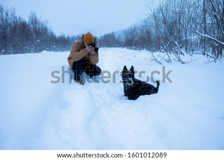 A man photographs his dog on winter walk in the snow.