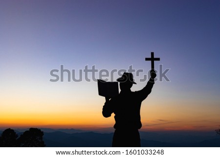 Human praying and holding christian cross for worshipping God at sunset sky background.Christian, Christianity, Religion copy space background. 