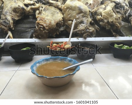 Mexican barbecue broth and golden tacos, cooked ram pieces ready to eat, dish in market with disposable spoon