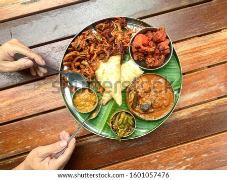 Man using fork and spoon to eat banana leaf dish, consists of fried chicken, curry seafood, lady fingerspotatoes and canai