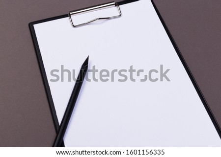 Clipboard with white sheet and pen on a colored background. View from above. space for text