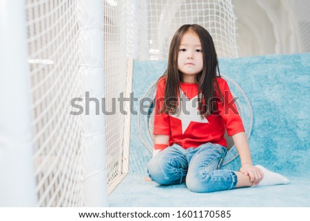 Pretty little Asian girl with long hair wearing costume of super girl looking at you on play area